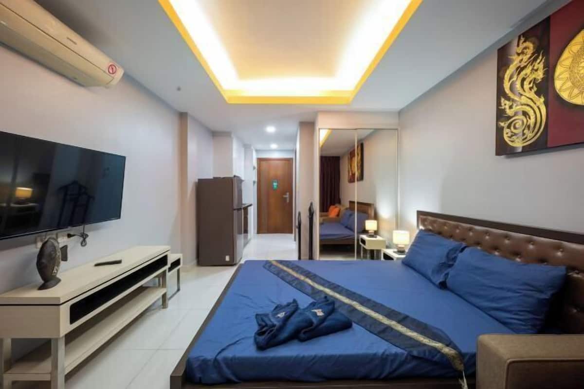 A hotel room with a bed, a TV, a mirror, and a door leading to a bathroom.