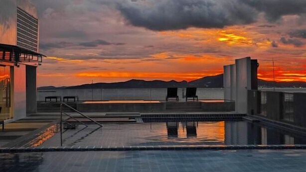 Una piscina sul tetto con vista sul tramonto, un edificio moderno e cielo sereno.
