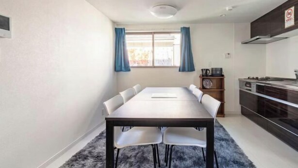 A modern kitchen with a dining area, a window with curtains, and a clock on the wall. - Coast Nishikōjiya (Tokyo)