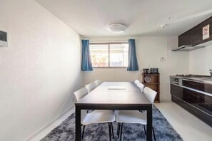 A modern kitchen with a dining area, a window with curtains, and a clock on the wall. - Coast Nishikōjiya (Tokyo)