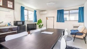 A modern room with a dark wooden table, white chairs, a small kitchenette, a sofa, and a potted plant. - Coast Nishikōjiya (Tokyo)