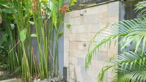 A stone shower enclosure with a tiled wall, surrounded by lush green plants and a small step leading up to it. - Puri Gading Villa Jimbaran by The Lavana (Bali)
