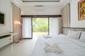 A hotel room with a bed, a TV, a desk, a lamp, and a view of a garden.