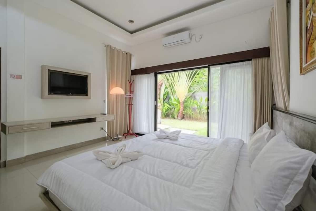 Habitación de hotel con cama, televisión, ventana con cortinas y vista a zonas verdes.