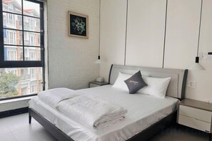 A hotel room with a bed, a nightstand, a lamp, a window with a view of buildings, and a framed picture on the wall. - My Anh 58 House Homestay (Haiphong)