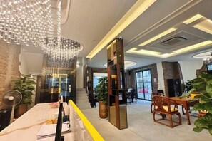 Un hall d’hôtel comprenant un comptoir d’accueil, un espace salon et un grand lustre.
