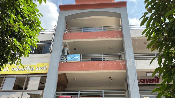 Un immeuble à plusieurs étages, avec une enseigne indiquant « Hôtel Radhe et maison d’hôtes » au deuxième étage.