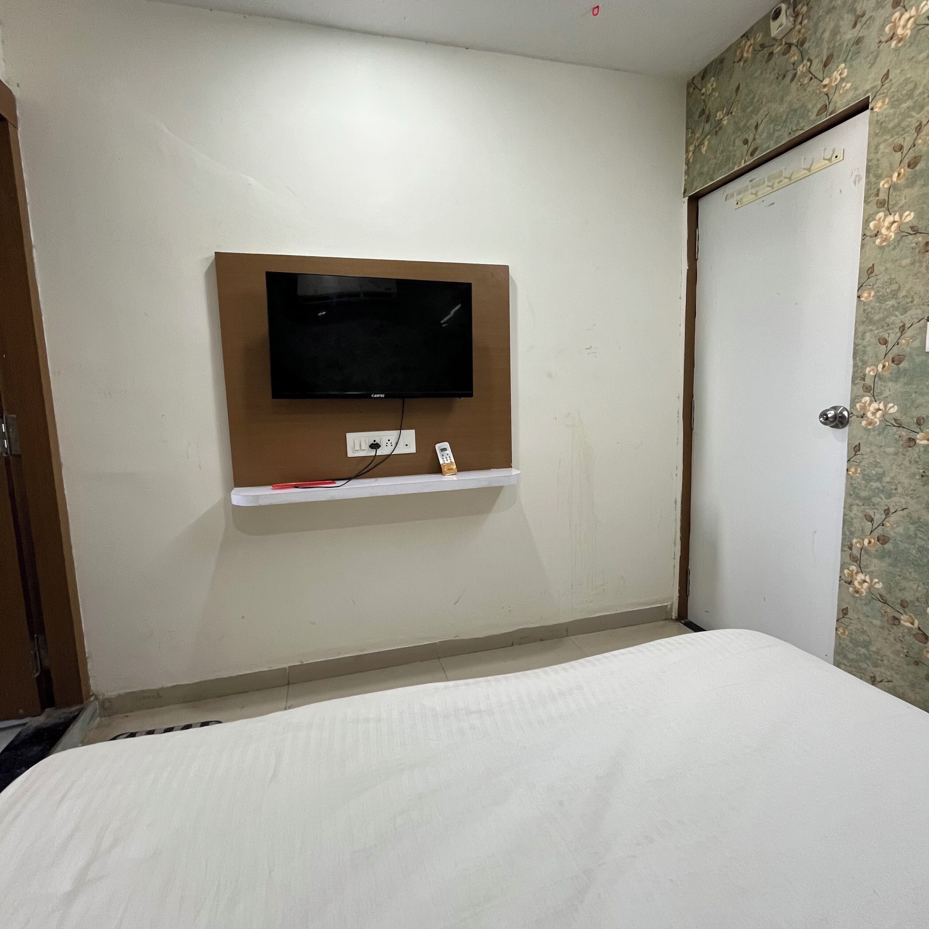Habitación de hotel con televisión de pantalla plana en la pared, un enchufe y un pequeño estante debajo.