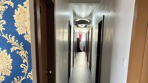 Un long couloir étroit, avec un tapis à motifs d’un côté et un sol carrelé de l’autre.
