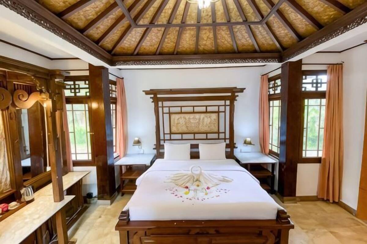 A traditional room with a wooden bed, a large mirror, and a ceiling with a wooden beam structure.