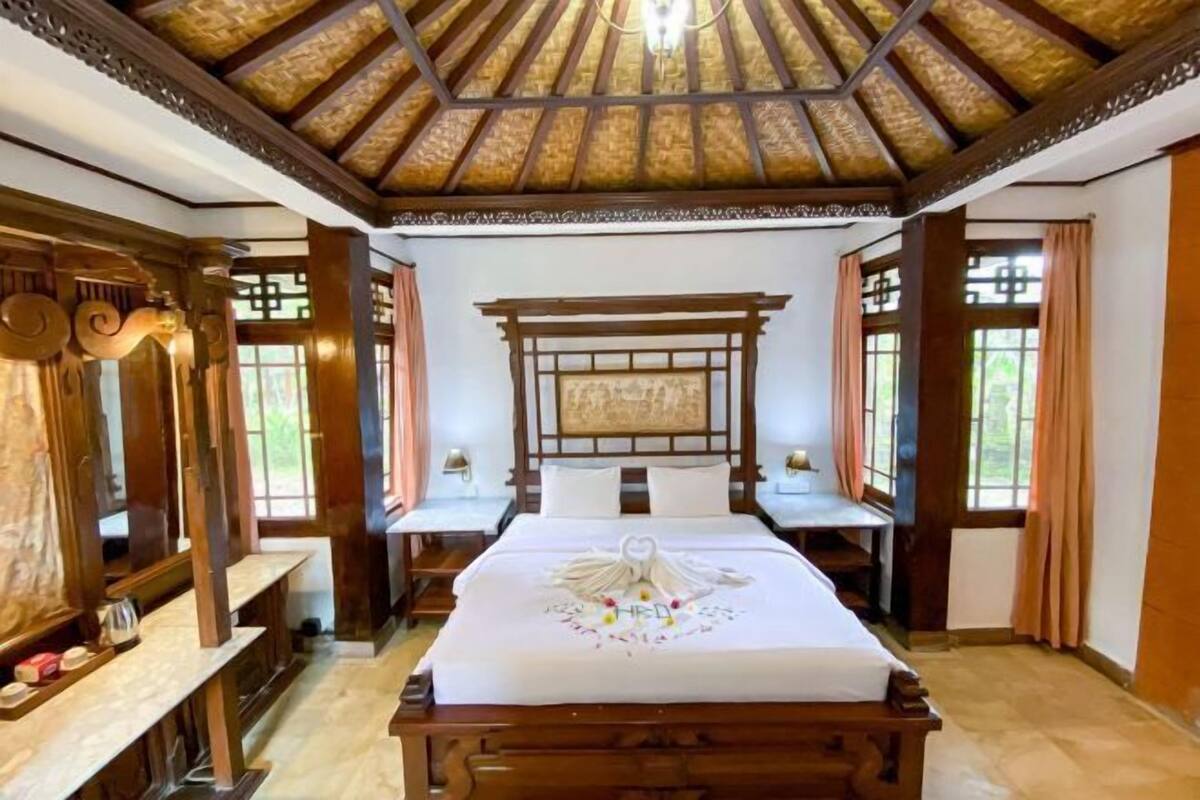A traditional-style bedroom with a wooden bed, a large window, and a ceiling with a wooden beam structure.