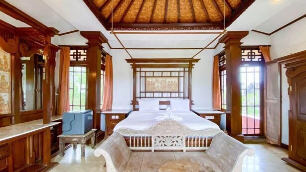 A traditional room with a wooden ceiling, a bed with a white headboard, and a stone bench. - RedDoorz @ Garden Suly Villa Peliatan Ubud (Bali)