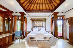A traditional room with a wooden ceiling, a bed with a white headboard, and a stone bench. - RedDoorz @ Garden Suly Villa Peliatan Ubud (Bali)