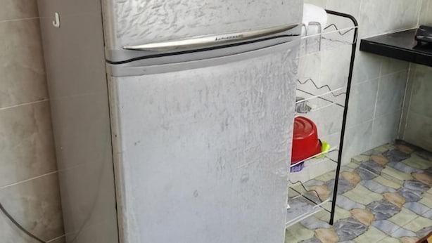 A kitchen with a refrigerator, a metal shelf, and a tiled floor. - Homestay Che Naa (Kuala Kuantan)