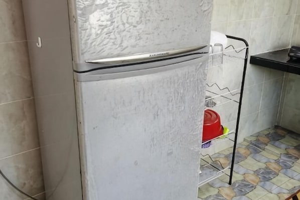 A kitchen with a refrigerator, a metal shelf, and a tiled floor. - Homestay Che Naa (Kuala Kuantan)