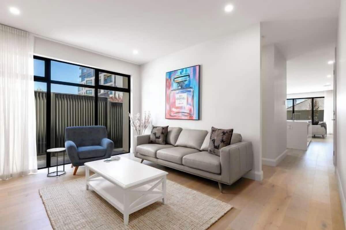 A modern living room with a sofa, armchair, coffee table, and a large window.
