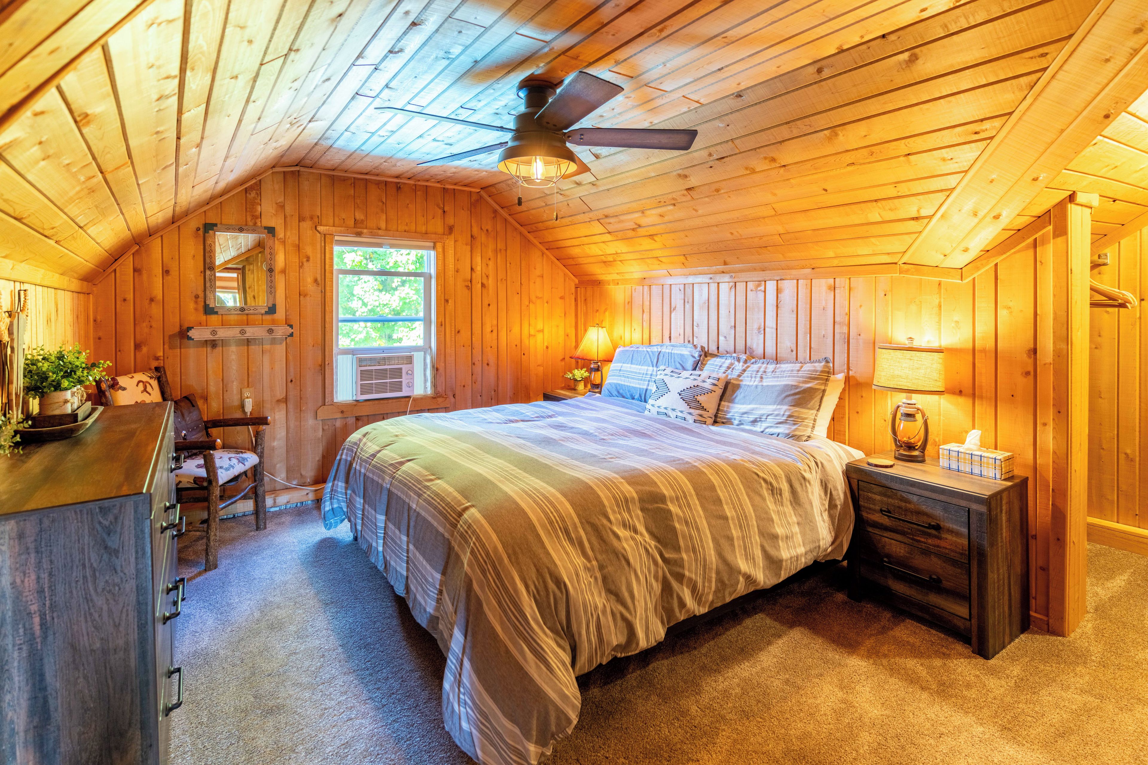 A cozy wooden room with a bed, a desk, a chair, and a window.