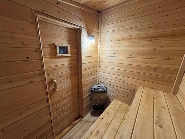 Una sauna de madera con puerta, un estante pequeño y un banco.