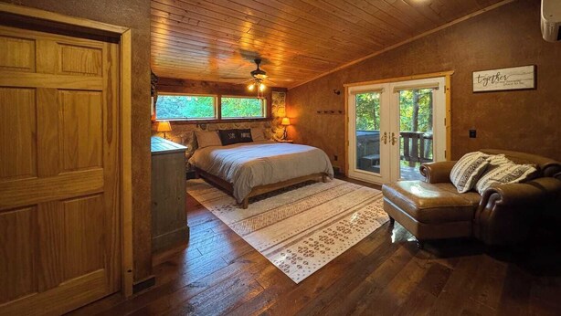 A cozy bedroom with a bed, a nightstand, a dresser, a window, and a sliding glass door leading to an outdoor area. - NEW! TC Ranch Therapy - Hot Tub, Sauna, Pool Table (Traverse City)