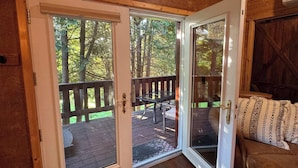 A cozy cabin interior with a wooden ceiling, a sliding glass door leading to an outdoor deck, and a comfortable seating area with a patterned rug. - NEW! TC Ranch Therapy - Hot Tub, Sauna, Pool Table (Traverse City)