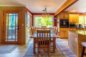 A spacious kitchen with wooden cabinets, a dining area with a large table and chairs, and a view of the outdoors through the windows.