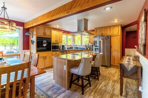 A spacious kitchen with wooden cabinets, a central island, and a dining area with chairs. - NEW! TC Ranch Therapy - Hot Tub, Sauna, Pool Table (Traverse City)
