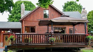A log cabin with a covered porch, stone chimneys, and a welcoming sign. - NEW! TC Ranch Therapy - Hot Tub, Sauna, Pool Table (Traverse City)