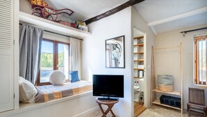 Une pièce comprenant un lit, un téléviseur posé sur un meuble, une fenêtre avec des rideaux, une bibliothèque et une chaise.
