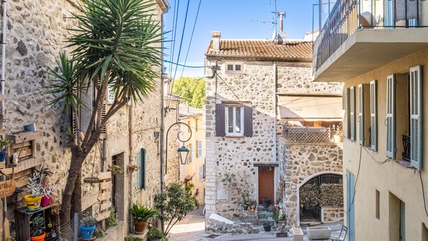 Une rue étroite bordée d’immeubles en pierre, de balcons et de plantes en pot.