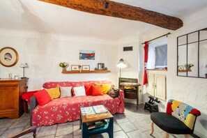 A cozy living room with a red floral sofa, a wooden coffee table, a small side table, and a colorful chair.