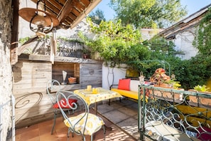 An outdoor patio with a wooden table, metal chairs, a yellow sofa, and potted plants.