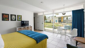 Une chambre d’hôtel avec un lit, une télévision, un balcon avec une table et des chaises, et une vue sur l’extérieur.