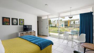 Une chambre d’hôtel avec un lit, une télévision, un balcon avec une table et des chaises, et une vue sur l’extérieur.