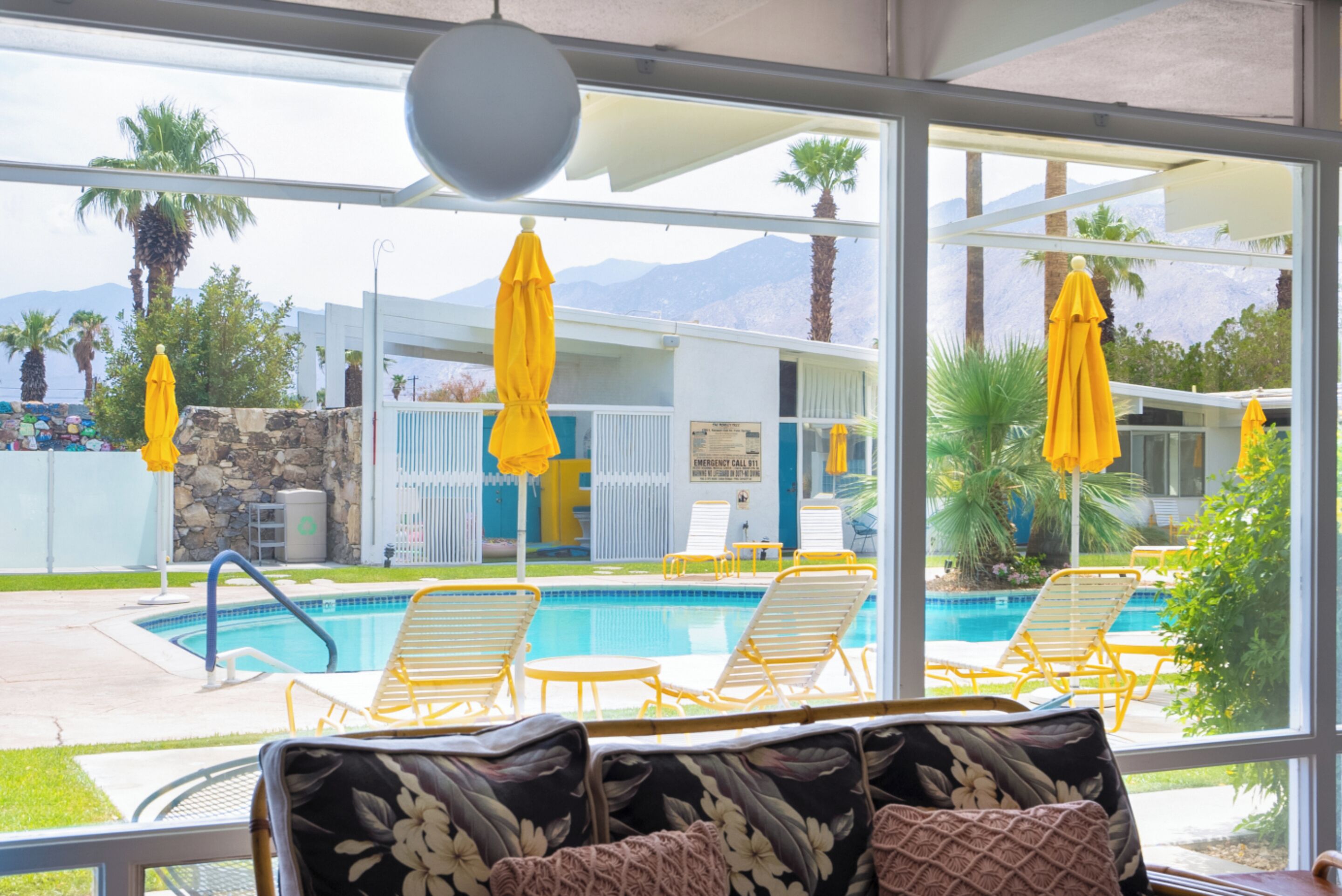 Un espace aménagé au bord de la piscine, avec des parasols jaunes, des chaises longues et une vue sur une chaîne de montagnes.