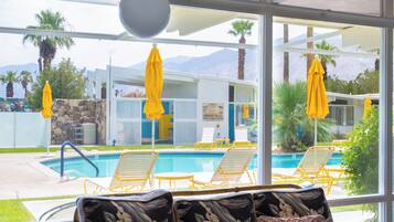 Un espace aménagé au bord de la piscine, avec des parasols jaunes, des chaises longues et une vue sur une chaîne de montagnes.