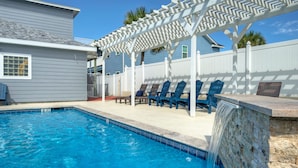 A swimming pool with a waterfall feature, surrounded by a white fence and blue chairs. - 2BDR Condo w/ Pool | Walk to Shore, Pet-Friendly (Port Aransas)