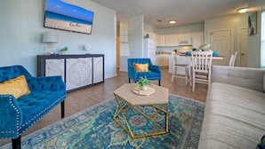 A living room with a sofa, two armchairs, a coffee table, and a TV mounted on the wall. - 2BDR Condo w/ Pool | Walk to Shore, Pet-Friendly (Port Aransas)