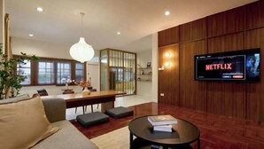A modern living room with a sofa, a round coffee table, a TV mounted on the wall, and a dining area with a table and chairs. - AIRI Home,3BR near Thapae and walking str old town CNX (Chiang Mai)