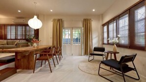 A spacious living area with a wooden dining table, chairs, a sofa, and a large window with blinds. - AIRI Home,3BR near Thapae and walking str old town CNX (Chiang Mai)