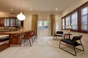 A spacious living area with a wooden dining table, chairs, a sofa, and a large window with blinds. - AIRI Home,3BR near Thapae and walking str old town CNX (Chiang Mai)