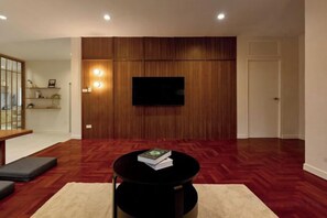 A living room with a flat-screen TV mounted on a wooden wall, a round black coffee table with a book, and a sofa. - AIRI Home,3BR near Thapae and walking str old town CNX (Chiang Mai)