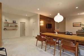 A modern dining area with a wooden table and chairs, a pendant light, and a television on the wall. - AIRI Home,3BR near Thapae and walking str old town CNX (Chiang Mai)