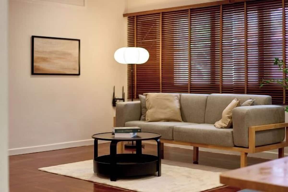 A living room with a sofa, a round coffee table, a lamp, and a window with blinds.