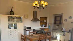 A dining area with a wooden table and chairs, a white cabinet with glass doors, a microwave, a stove, and a chandelier. - Marino House (Tuoro Sul Trasimeno)