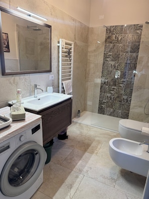A bathroom with a washing machine, a sink, a toilet, and a shower area.