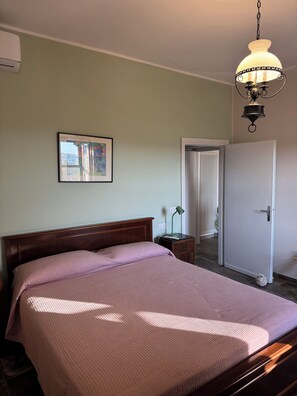Une chambre à coucher avec un lit, une table de chevet, une lampe, une porte et un tableau encadré au mur.