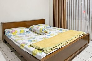 Uma cama com colcha florida, manta amarela e cabeceira de madeira.
