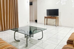 A living room with a glass-top table, a TV on a wooden stand, and a sofa. - Large Villa 3BR Cieumbuleuit near PVJ & Cihamplas (Cidadap)