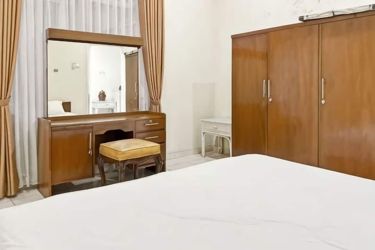 A bedroom with a bed, a wooden dresser with a mirror, a small stool, and a wardrobe.