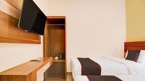 A hotel room with a bed, a wooden desk, a television mounted on the wall, and a closet. - Capital O Pusat Kota Pekanbaru Near Mall Living World Formerly Radja Homestay (Tengkerang Barat)